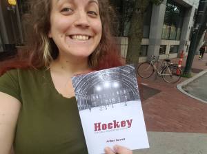 A white woman smiling cheesily and holding up a book called Hockey: Canada's Royal Winter Game